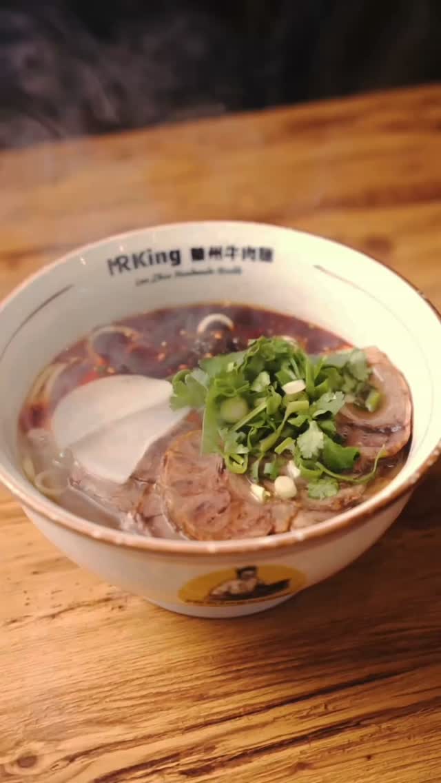 Steaming bowl of Lanzhou beef noodle soup with sliced beef, radish and fresh coriander on a wooden table